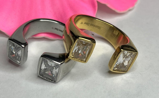 Anello Geometric Luxury con design geometrico quadrato, disponibile in versione placcata oro e argento, esposto su fiore rosa decorativo