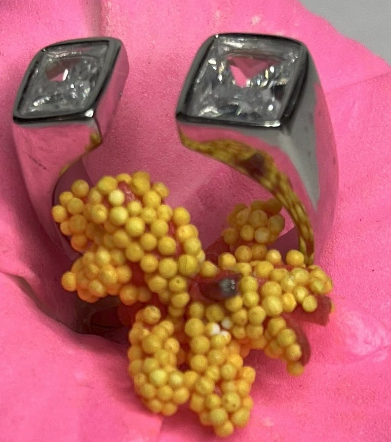 Anello Geometric Luxury con design geometrico quadrato, disponibile in versione placcata oro e argento, esposto su fiore rosa decorativo