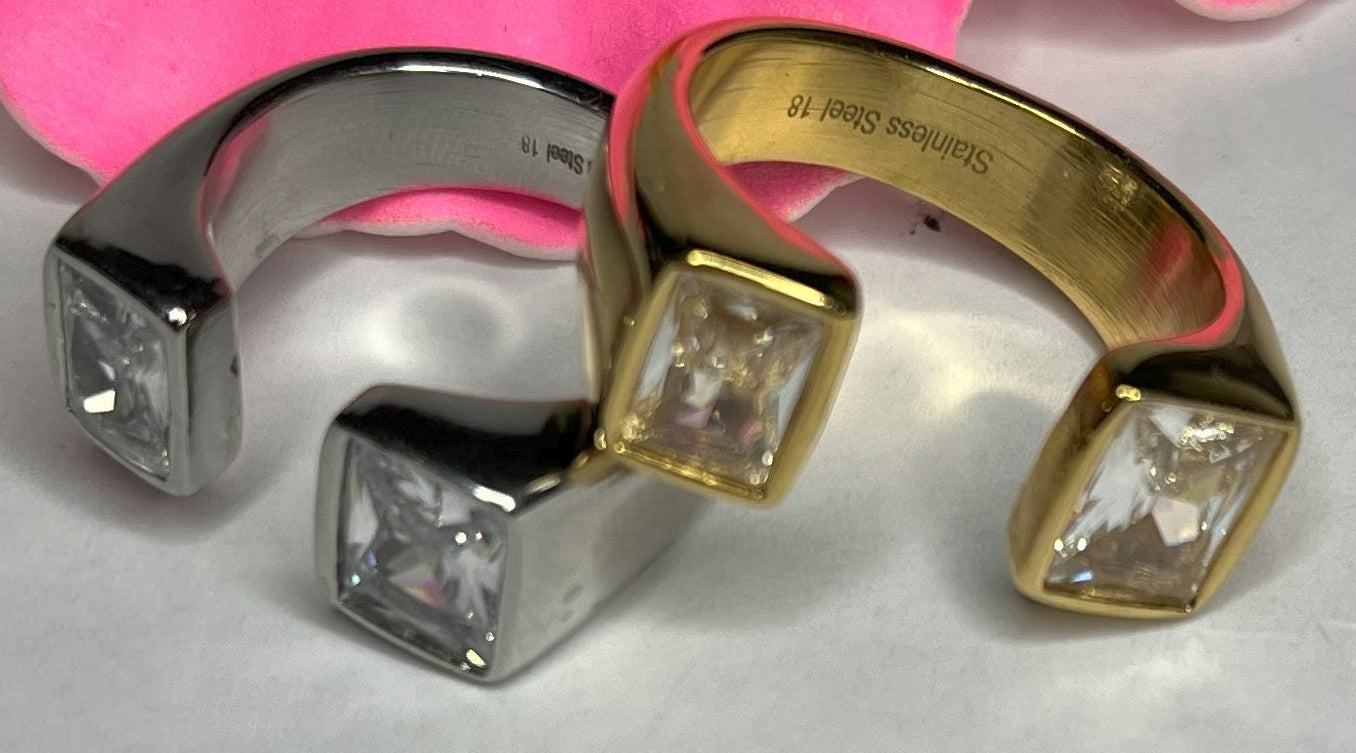 Anello Geometric Luxury con design geometrico quadrato, disponibile in versione placcata oro e argento, esposto su fiore rosa decorativo