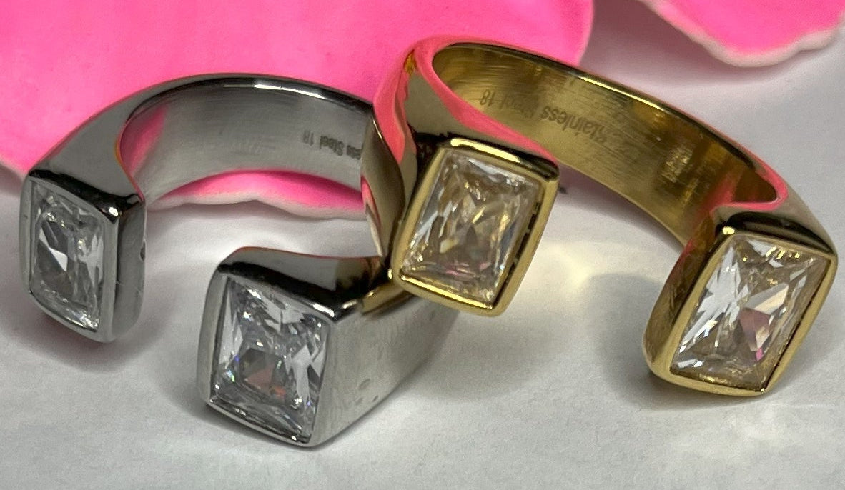 Anello Geometric Luxury con design geometrico quadrato, disponibile in versione placcata oro e argento, esposto su fiore rosa decorativo