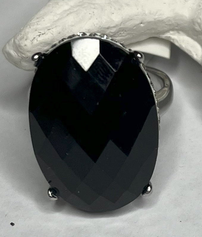 Anello con pietra nera ovale lucida e montatura argentata o dorata decorata, appoggiato su stella marina bianca