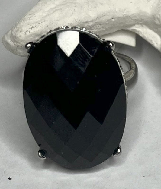 Anello con pietra nera ovale lucida e montatura argentata o dorata decorata, appoggiato su stella marina bianca