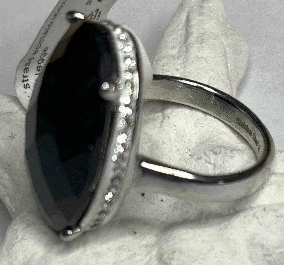 Anello con pietra nera ovale lucida e montatura argentata o dorata decorata, appoggiato su stella marina bianca