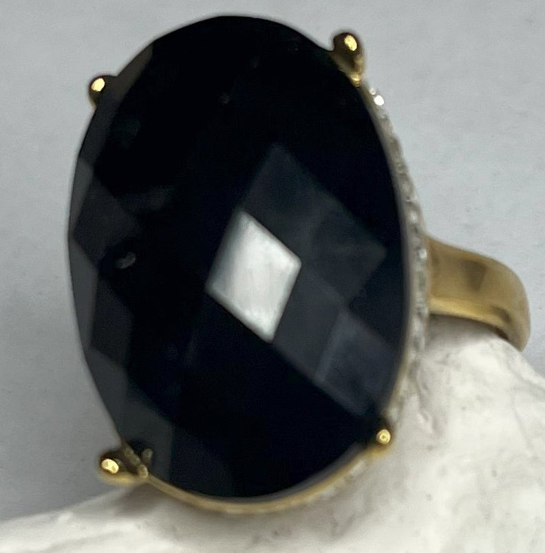 Anello con pietra nera ovale lucida e montatura argentata o dorata decorata, appoggiato su stella marina bianca
