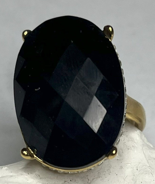 Anello con pietra nera ovale lucida e montatura argentata o dorata decorata, appoggiato su stella marina bianca