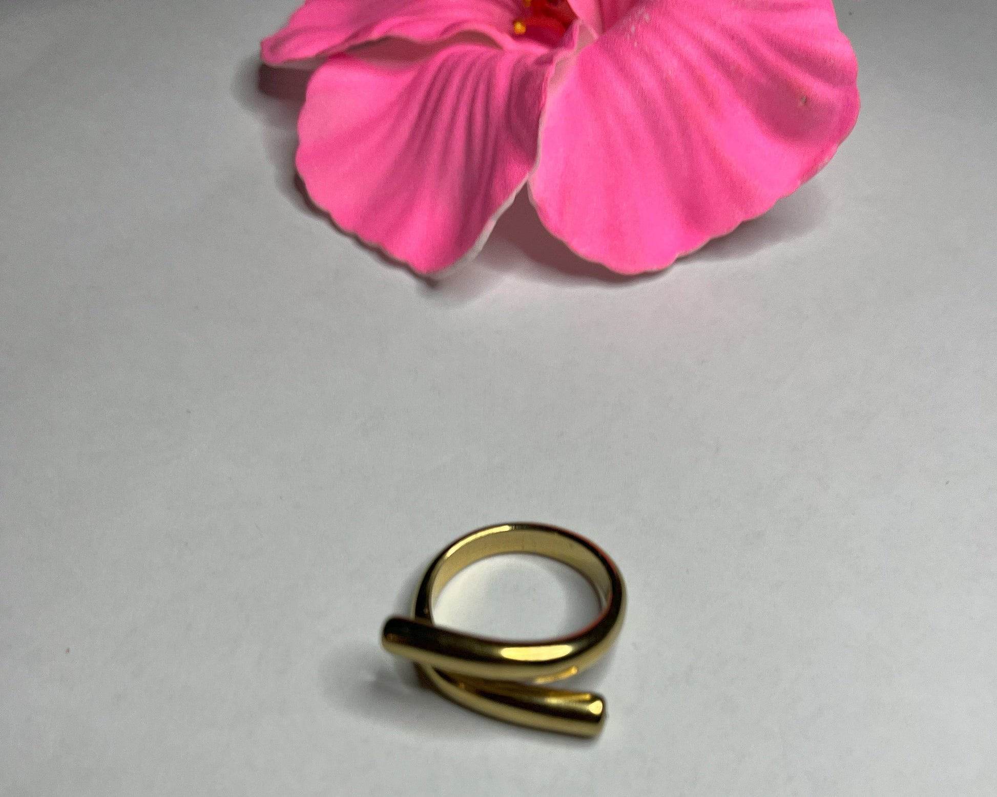 Anello Twist in acciaio premium con design avvolgente moderno, in placcatura oro, fotografato su sfondo neutro con petali rosa per evidenziare l'eleganza contemporanea