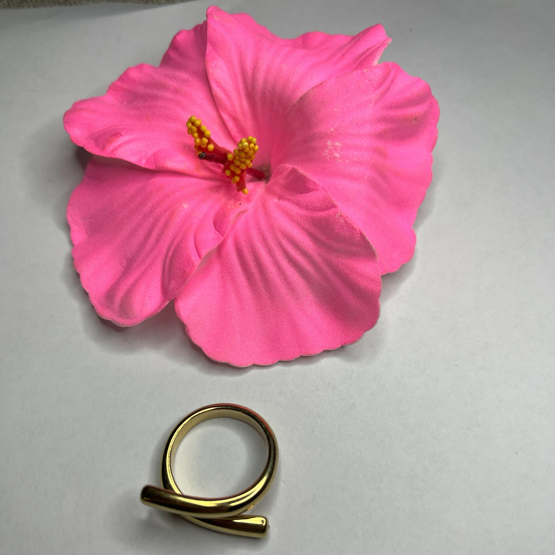 Anello Twist in acciaio premium con design avvolgente moderno, in placcatura oro, fotografato su sfondo neutro con petali rosa per evidenziare l'eleganza contemporanea