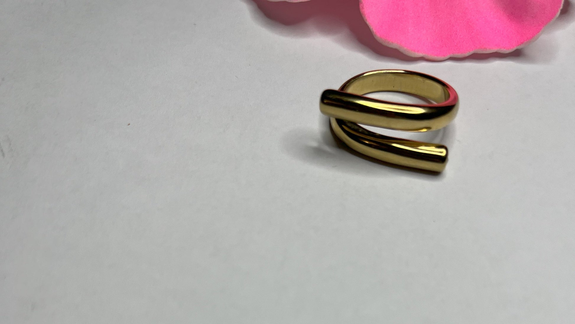 Anello Twist in acciaio premium con design avvolgente moderno, in placcatura oro, fotografato su sfondo neutro con petali rosa per evidenziare l'eleganza contemporanea