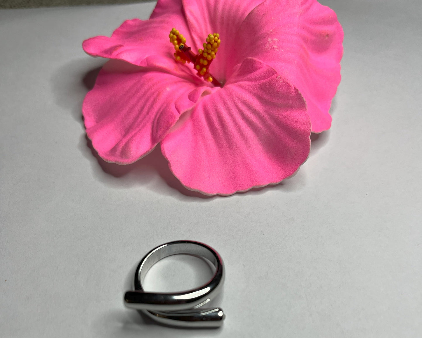 Anello Twist in acciaio premium con design avvolgente moderno, in placcatura argento, fotografato su sfondo neutro con petali rosa per evidenziare l'eleganza contemporanea