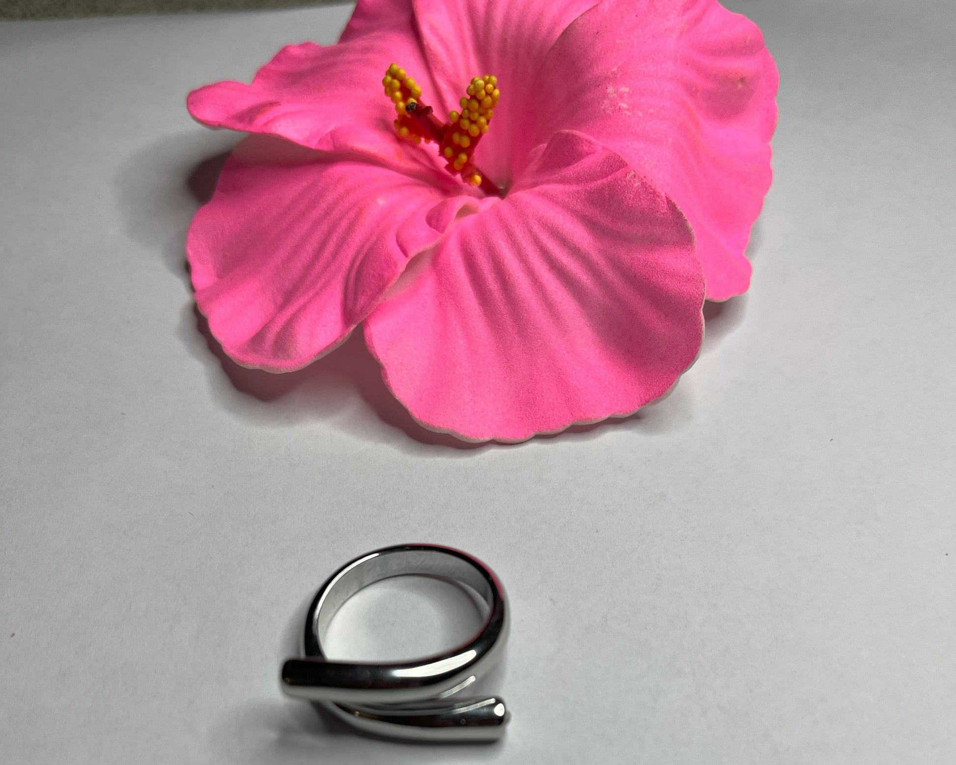 Anello Twist in acciaio premium con design avvolgente moderno, in placcatura argento, fotografato su sfondo neutro con petali rosa per evidenziare l'eleganza contemporanea