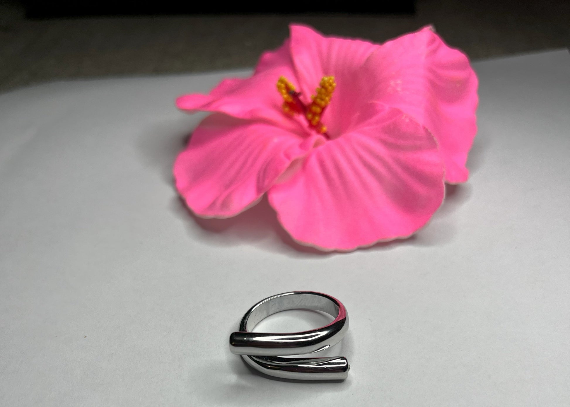 Anello Twist in acciaio premium con design avvolgente moderno, in placcatura oro, fotografato su sfondo neutro con petali rosa per evidenziare l'eleganza contemporanea