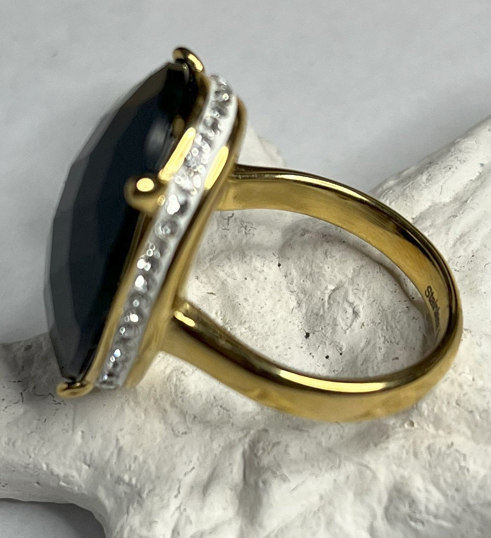 Anello con pietra nera ovale lucida e montatura argentata o dorata decorata, appoggiato su stella marina bianca