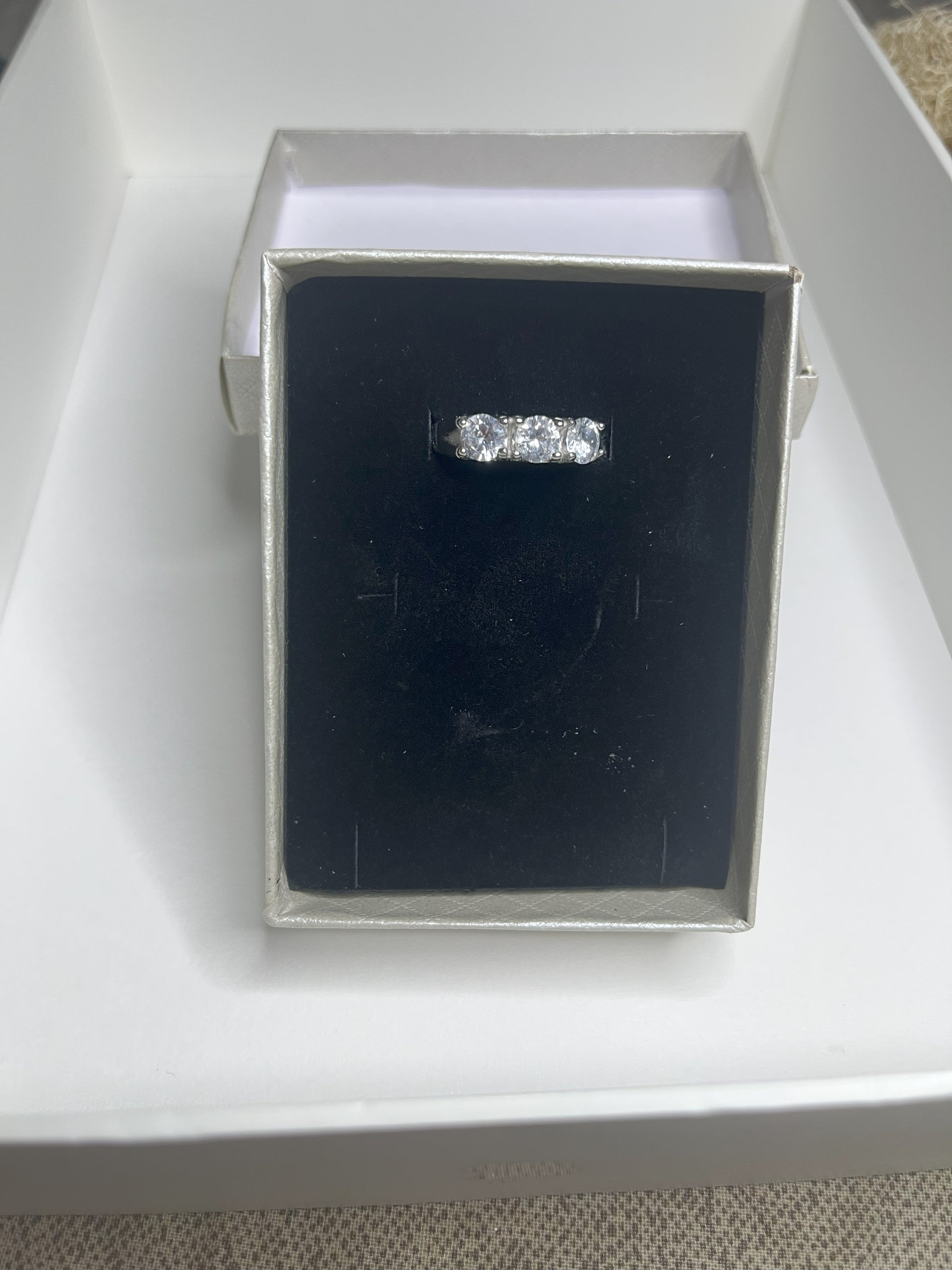 Anello Trio in acciaio premium placcato argento con tre zirconi brillanti perfettamente incastonati, fotografato su superficie scura che esalta la brillantezza delle pietre