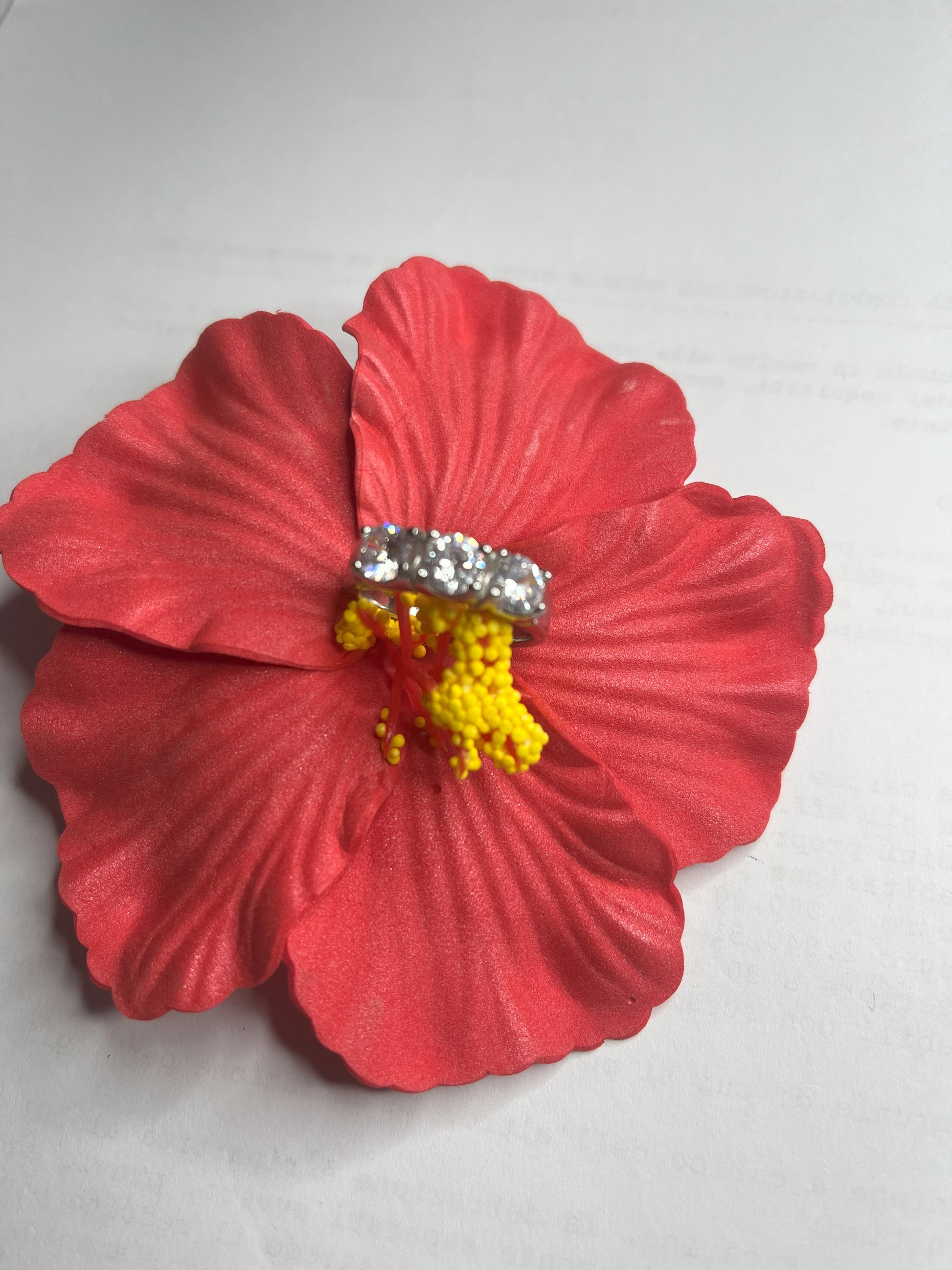 Anello Trio in acciaio premium placcato argento con tre zirconi brillanti perfettamente incastonati, fotografato su fiore rosso