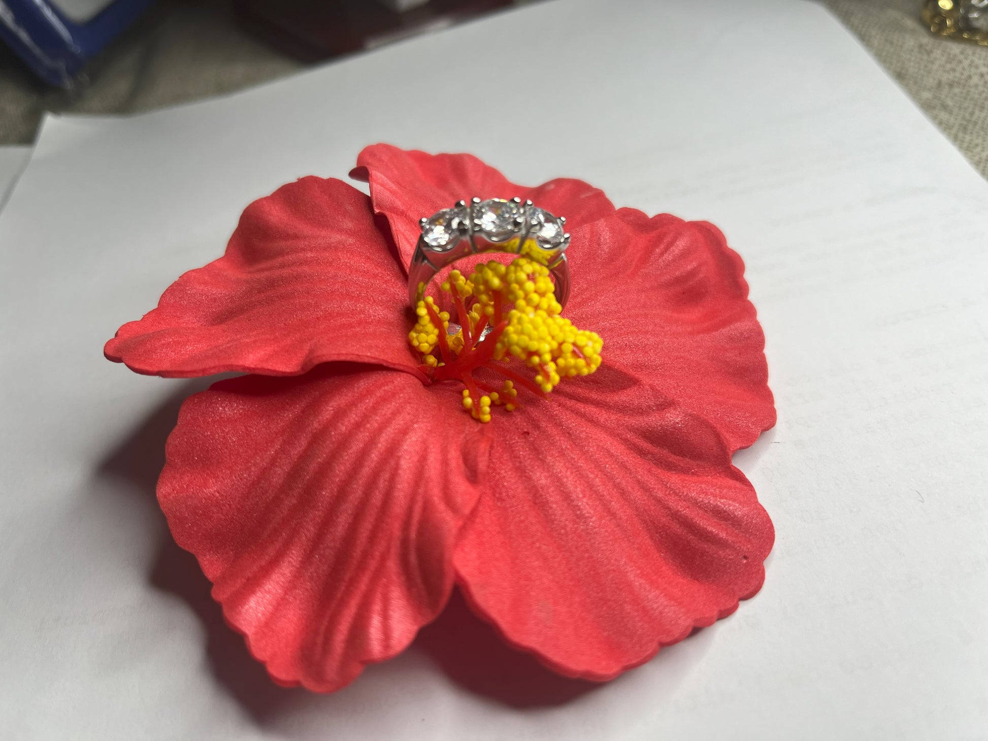 Anello Trio in acciaio premium placcato argento con tre zirconi brillanti perfettamente incastonati, fotografato su fiore rosso