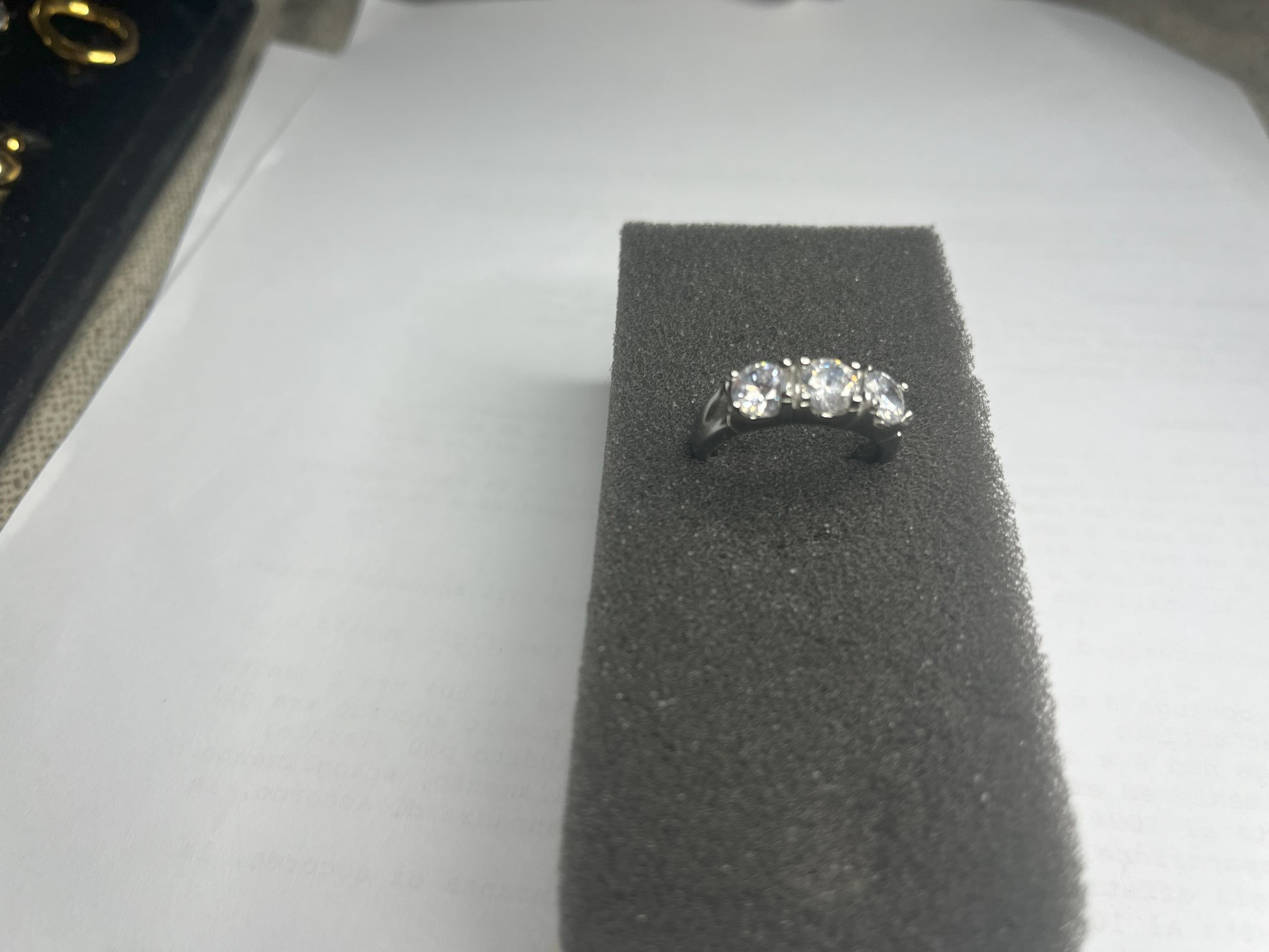Anello Trio in acciaio premium placcato argento con tre zirconi brillanti perfettamente incastonati, fotografato su superficie scura che esalta la brillantezza delle pietre