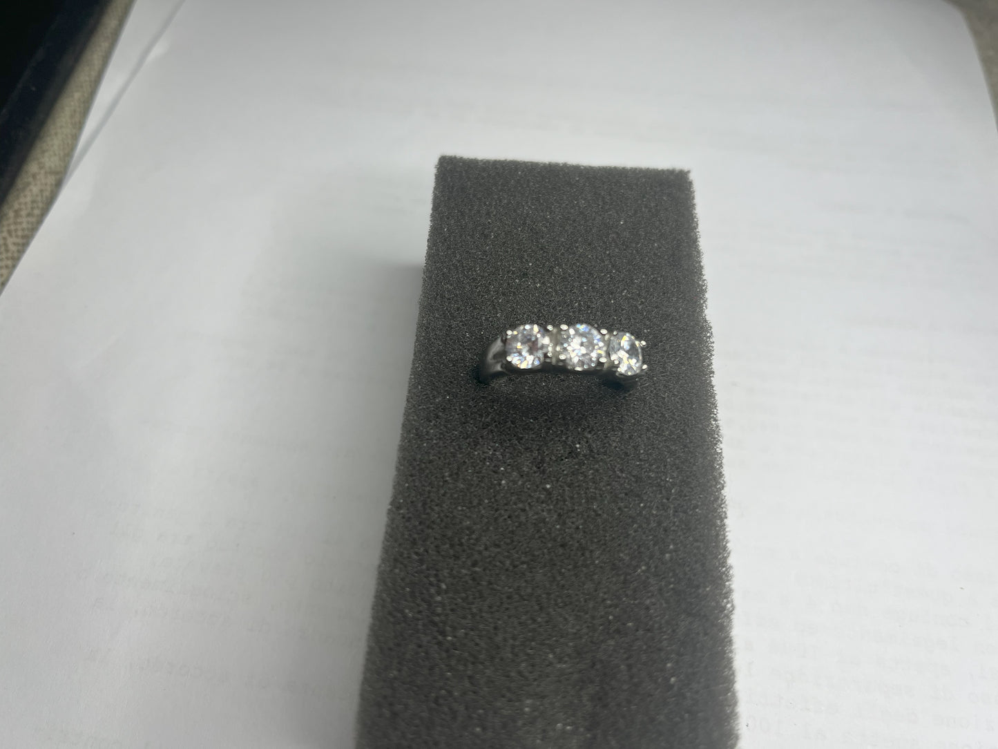 Anello Trio in acciaio premium placcato argento con tre zirconi brillanti perfettamente incastonati, fotografato su superficie scura che esalta la brillantezza delle pietre