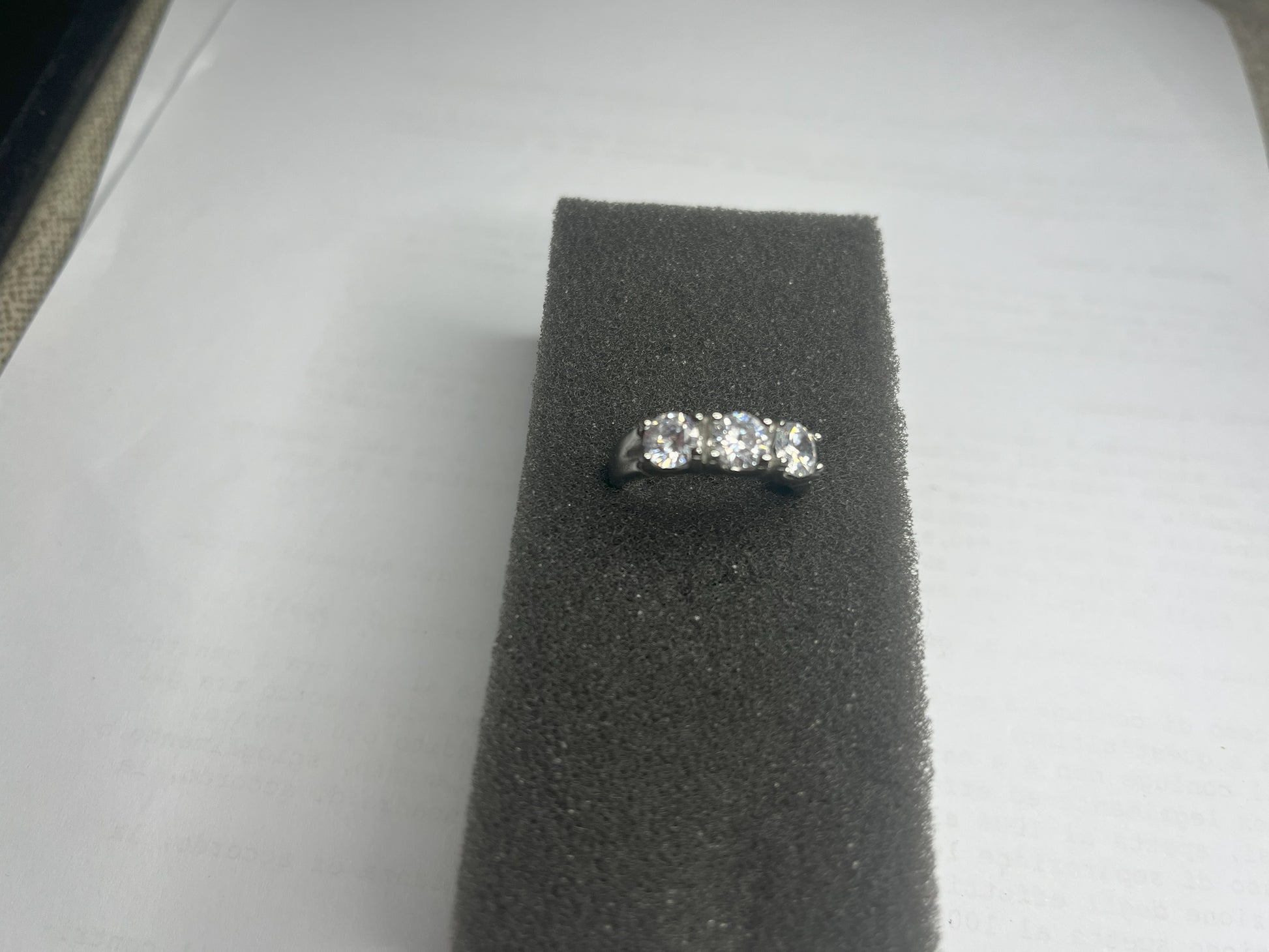Anello Trio in acciaio premium placcato argento con tre zirconi brillanti perfettamente incastonati, fotografato su superficie scura che esalta la brillantezza delle pietre