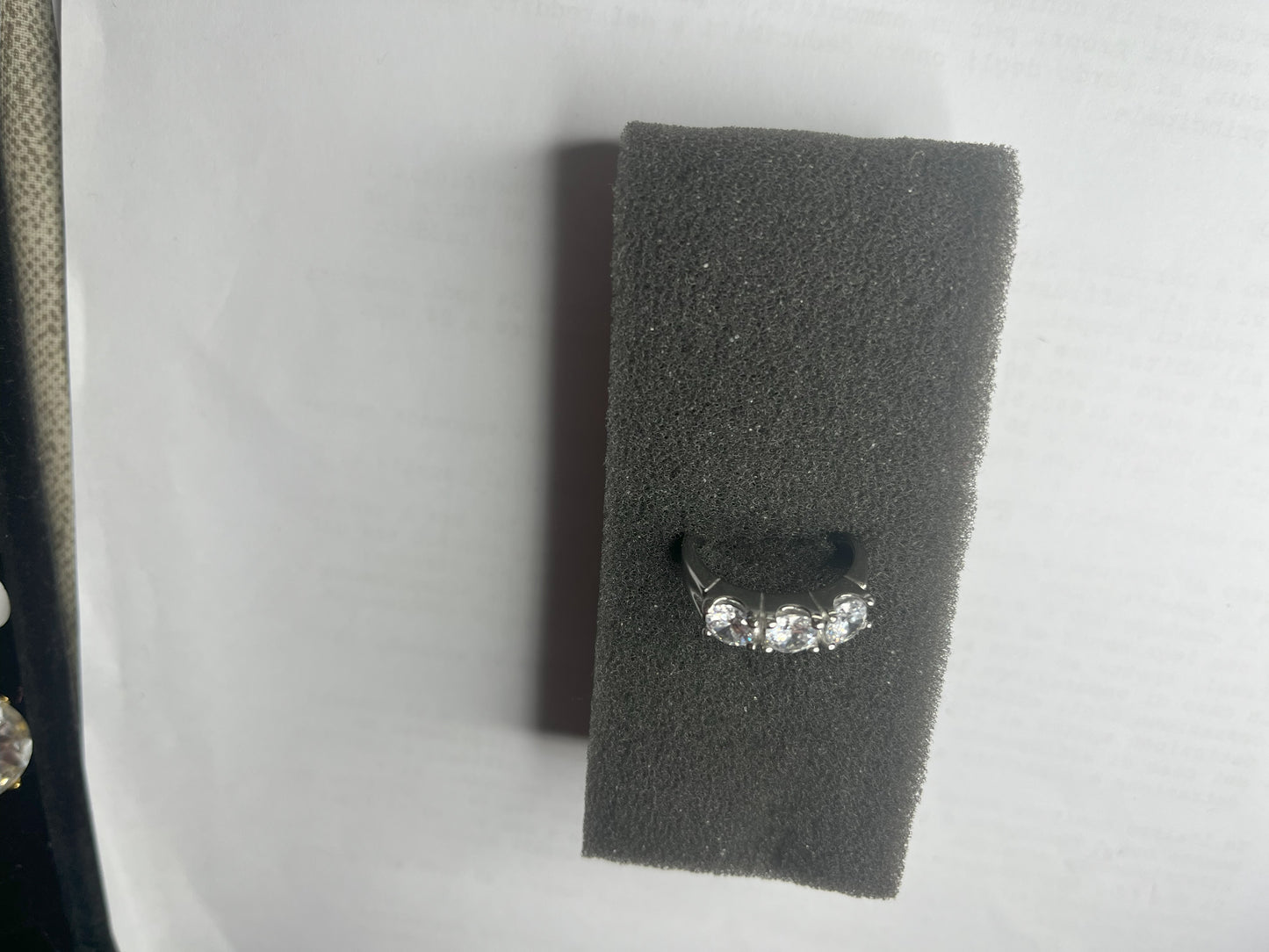 Anello Trio in acciaio premium placcato argento con tre zirconi brillanti perfettamente incastonati, fotografato su superficie scura che esalta la brillantezza delle pietre