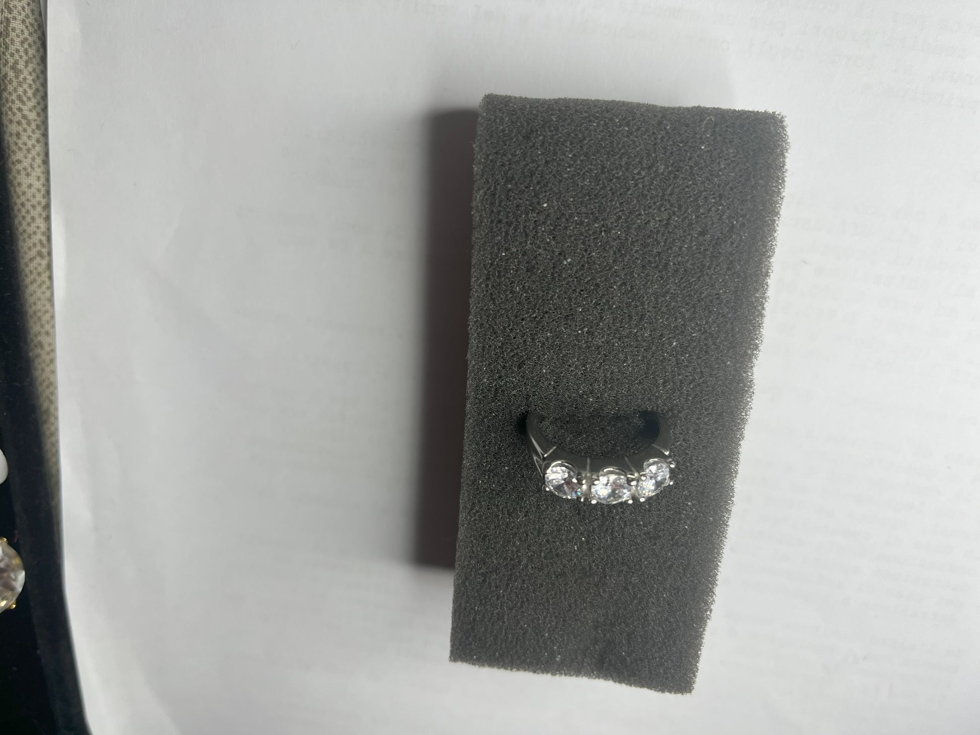 Anello Trio in acciaio premium placcato argento con tre zirconi brillanti perfettamente incastonati, fotografato su superficie scura che esalta la brillantezza delle pietre
