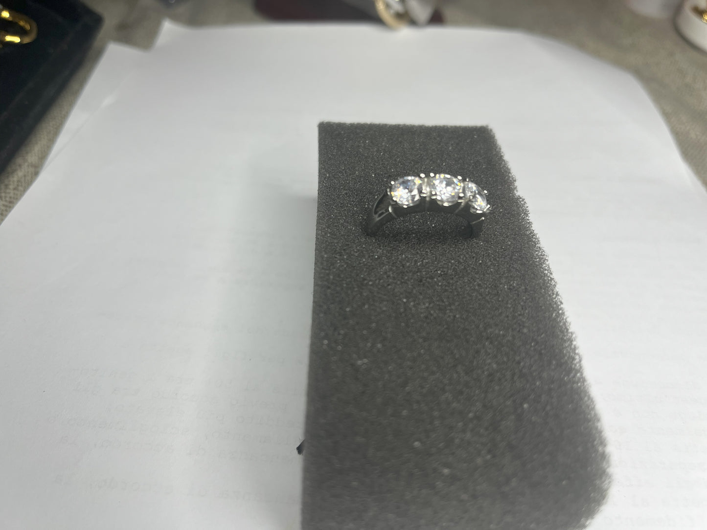 Anello Trio in acciaio premium placcato argento con tre zirconi brillanti perfettamente incastonati, fotografato su superficie scura che esalta la brillantezza delle pietre