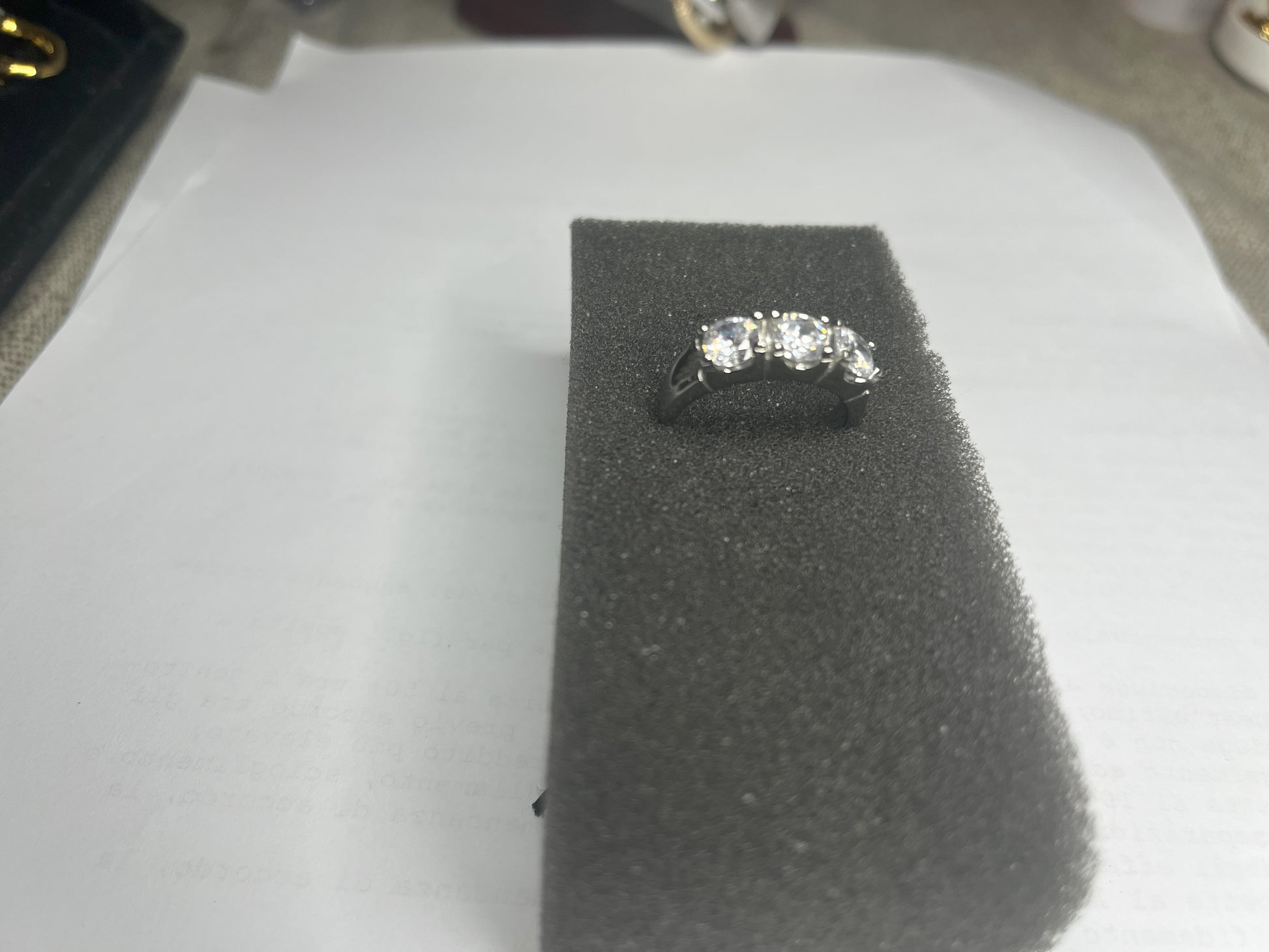 Anello Trio in acciaio premium placcato argento con tre zirconi brillanti perfettamente incastonati, fotografato su superficie scura che esalta la brillantezza delle pietre