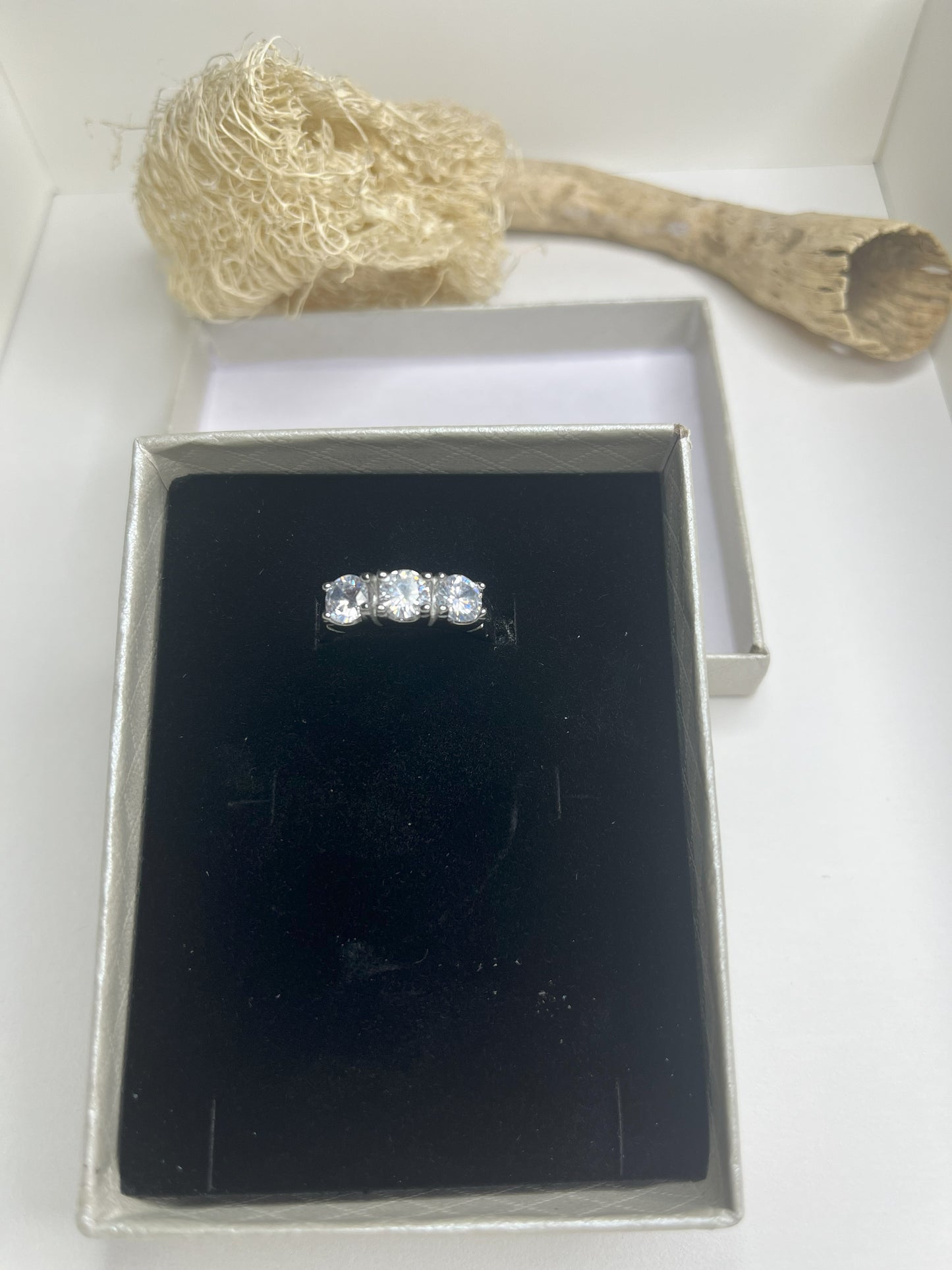 Anello Trio in acciaio premium placcato argento con tre zirconi brillanti perfettamente incastonati, fotografato su superficie scura che esalta la brillantezza delle pietre