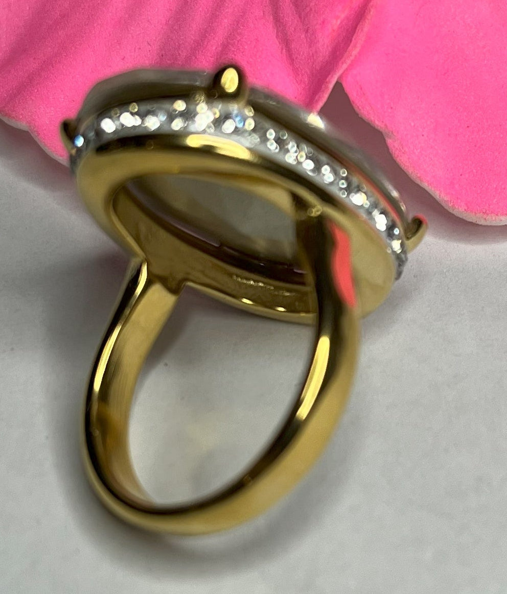Anello con pietra trasparente ovale lucida e montatura argentata o dorata decorata, appoggiato fiore fucsia