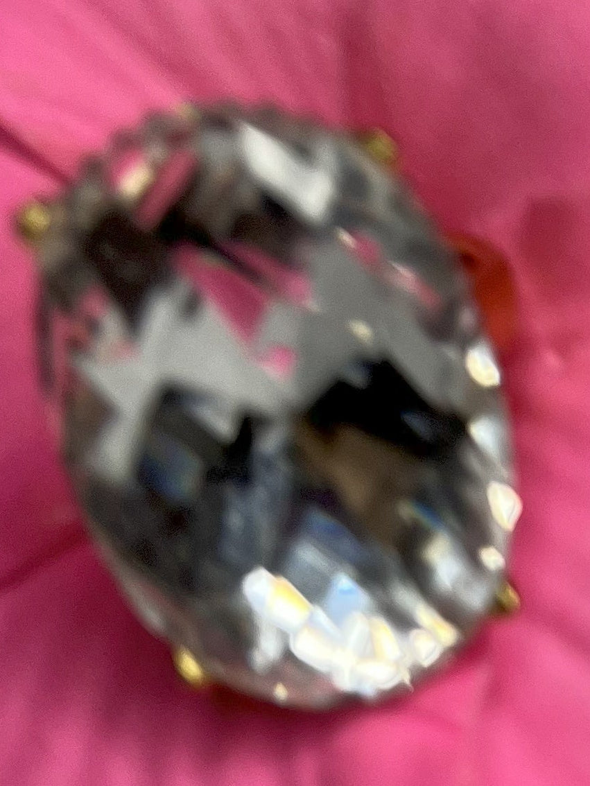 Anello con pietra trasparente ovale lucida e montatura argentata o dorata decorata, appoggiato fiore fucsia