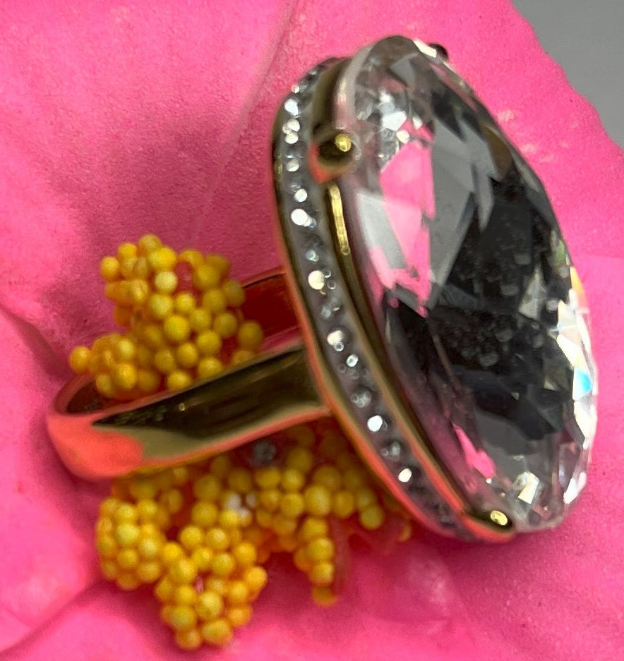 Anello con pietra trasparente ovale lucida e montatura argentata o dorata decorata, appoggiato fiore fucsia
