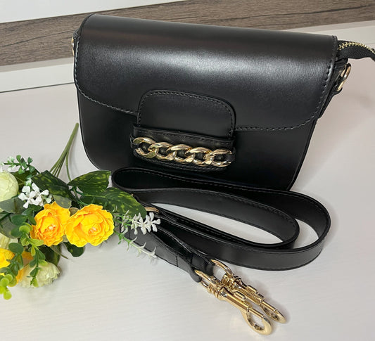 Borsa Toscana Chic in vera pelle nera Made in Italy con catena dorata decorativa e tracolla regolabile, fotografata su superficie bianca con fiori gialli