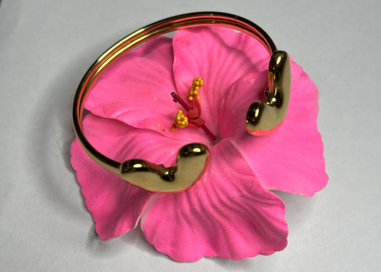 Braccialetto Due Cuori in acciaio premium placcato oro con design aperto regolabile, fotografato su fiore rosa fucsia per evidenziare l'eleganza romantica del gioiello