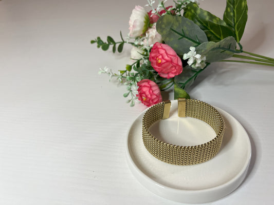 Braccialetto Cocò-G con elegante maglia dorata mesh e chiusura magnetica, esposto su piatto bianco con decorazioni floreali rosa