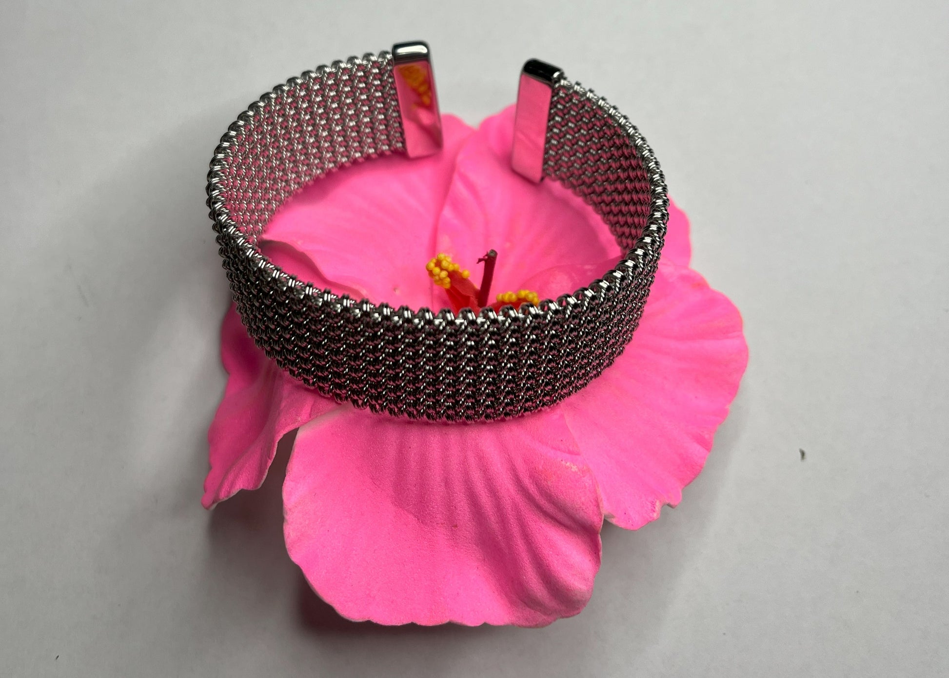 Braccialetto Cocò-G con elegante maglia dorata mesh e chiusura magnetica, esposto su piatto bianco con decorazioni floreali rosa