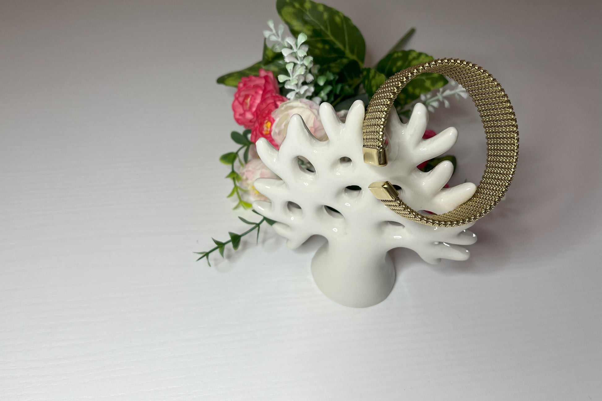 Braccialetto Cocò-G con elegante maglia dorata mesh e chiusura magnetica, esposto su piatto bianco con decorazioni floreali rosa