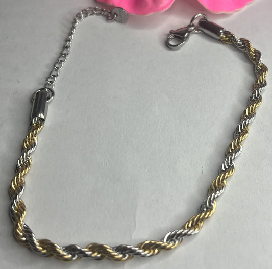 Braccialetto corda intrecciata bicolore oro e argento con chiusura metallica su sfondo grigio con petali rosa