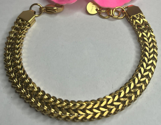 Braccialetto maglia cubana placcato oro con chiusura dorata su sfondo grigio con petali rosa