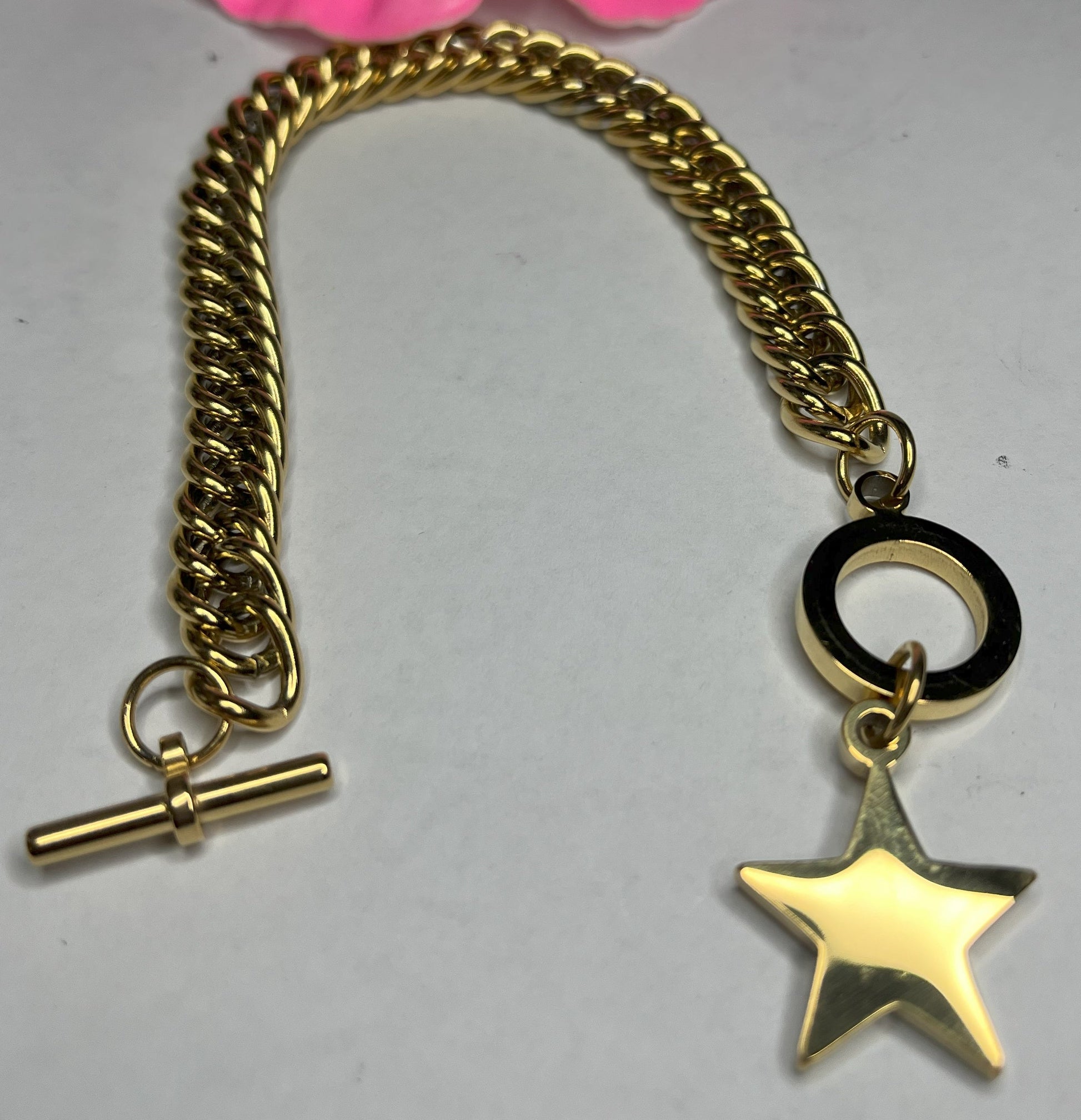 Braccialetto chunky placcato oro con pendente stella e chiusura toggle su sfondo grigio con petali rosa