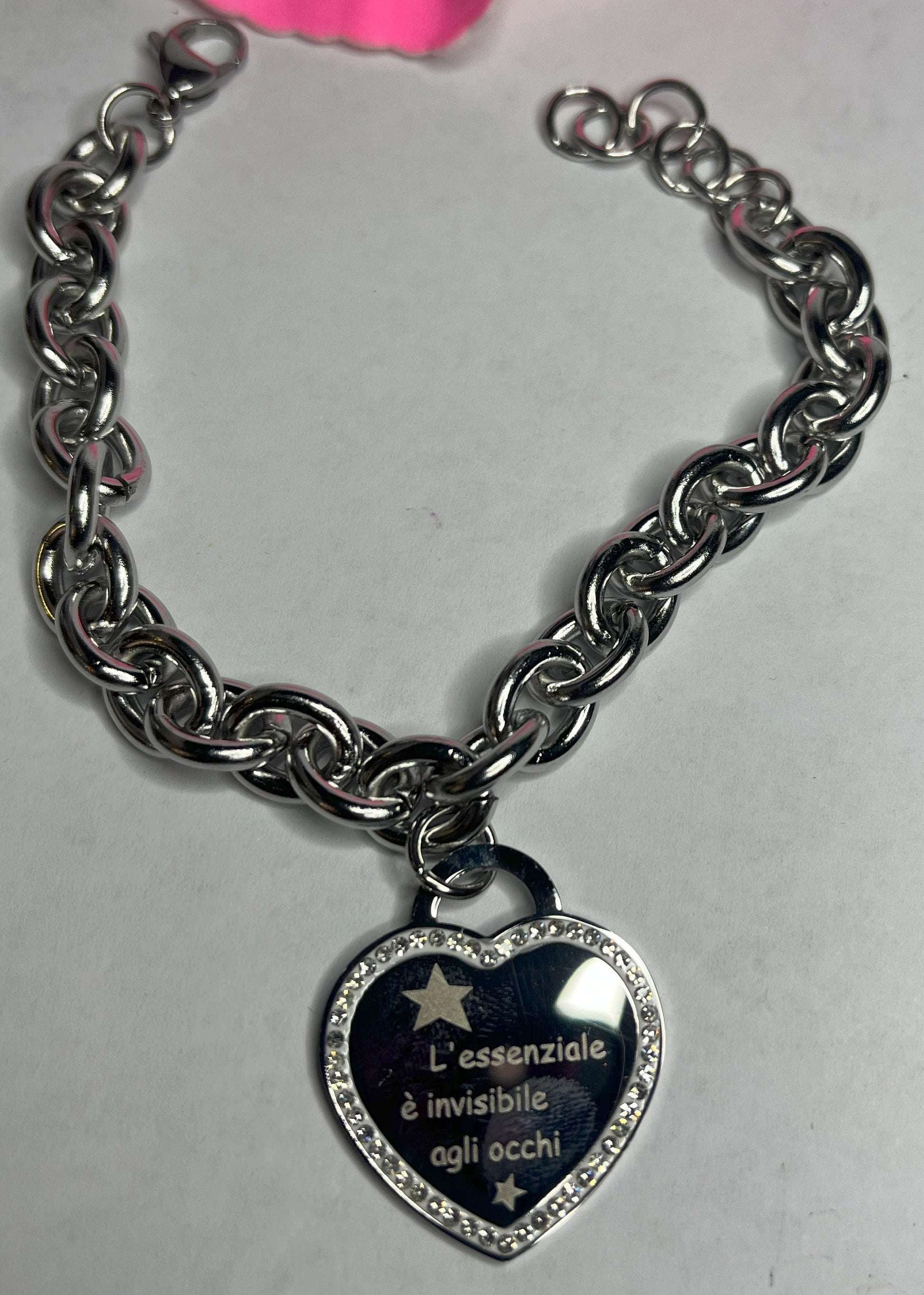 Braccialetto chunky argentato con pendente a cuore nero contenente la scritta "L'essenziale è invisibile agli occhi" su sfondo grigio con petali rosa