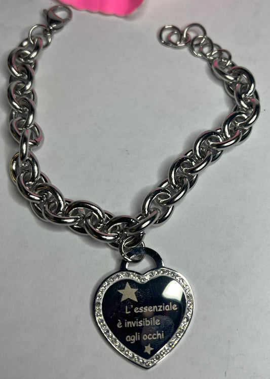 Braccialetto chunky argentato con pendente a cuore nero contenente la scritta "L'essenziale è invisibile agli occhi" su sfondo grigio con petali rosa
