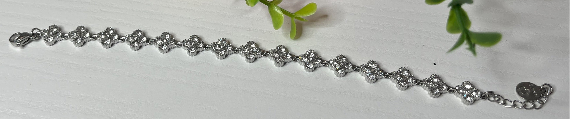 Braccialetto tennis placcato argento con quadrifogli portafortuna e cristalli scintillanti su sfondo bianco con foglie verdi
