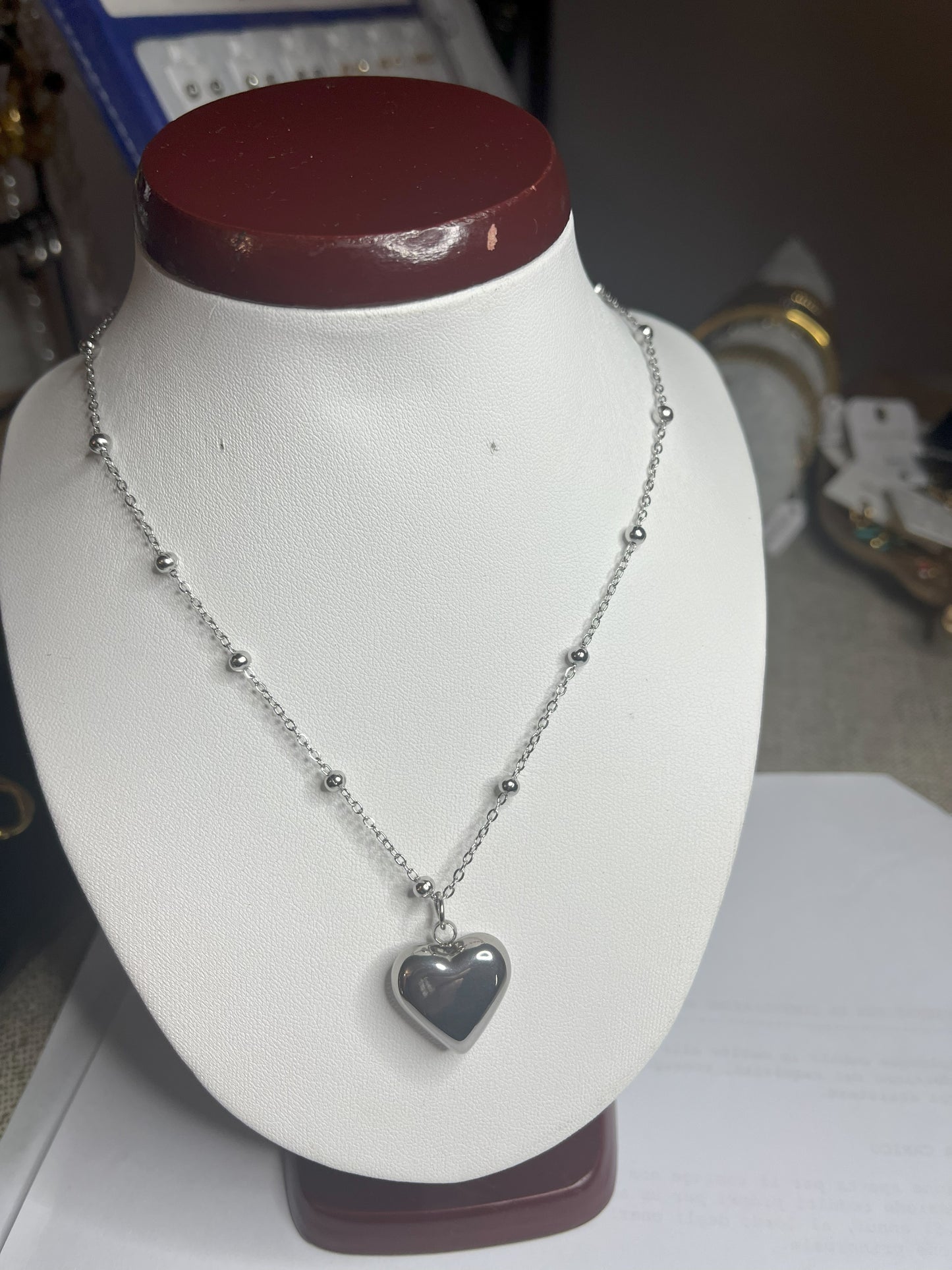 Collana Allegra in acciaio premium con catena decorata da sfere e ciondolo cuore, variante placcato argento, esposta su busto espositore bianco