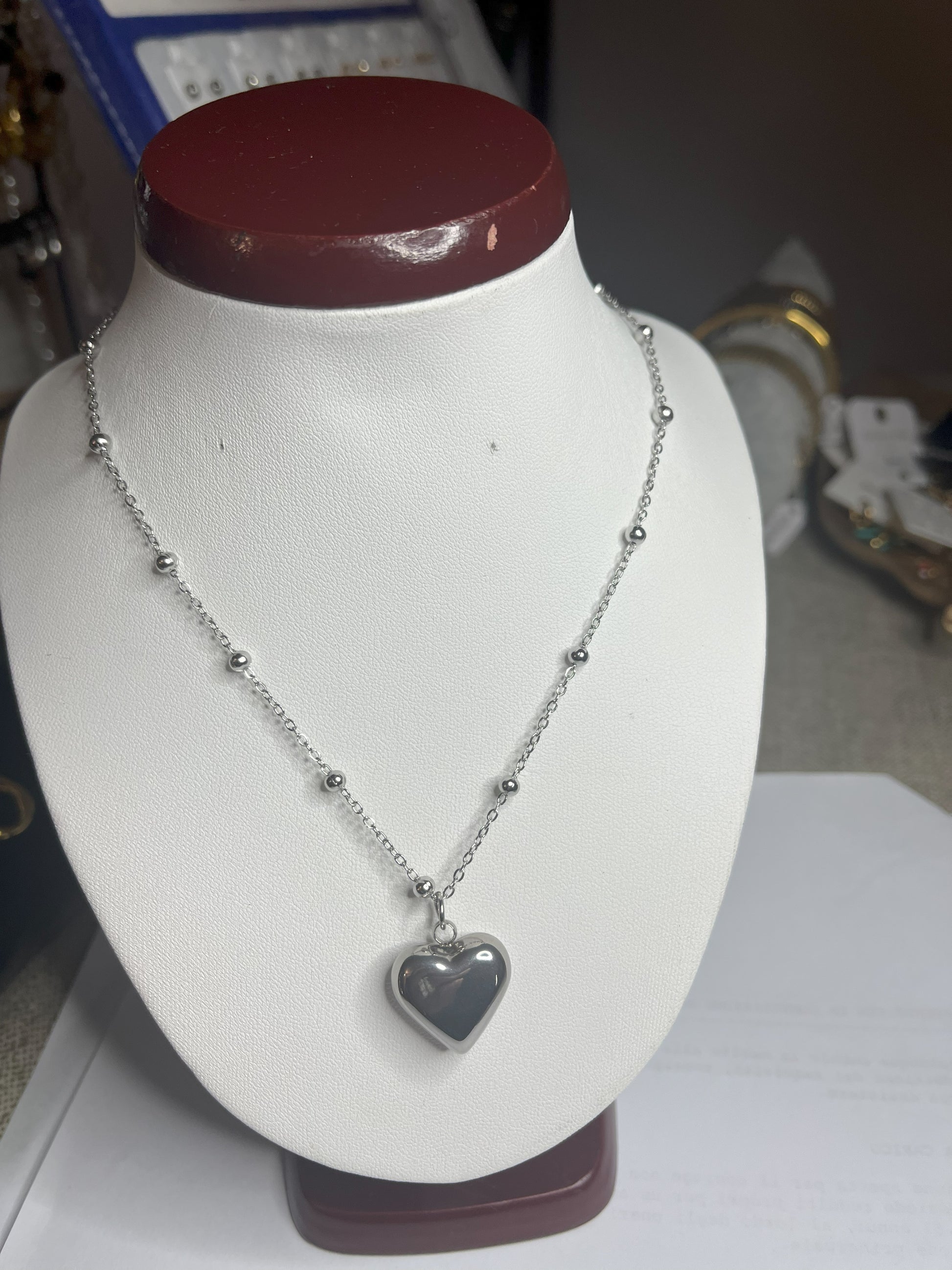 Collana Allegra in acciaio premium con catena decorata da sfere e ciondolo cuore, variante placcato argento, esposta su busto espositore bianco