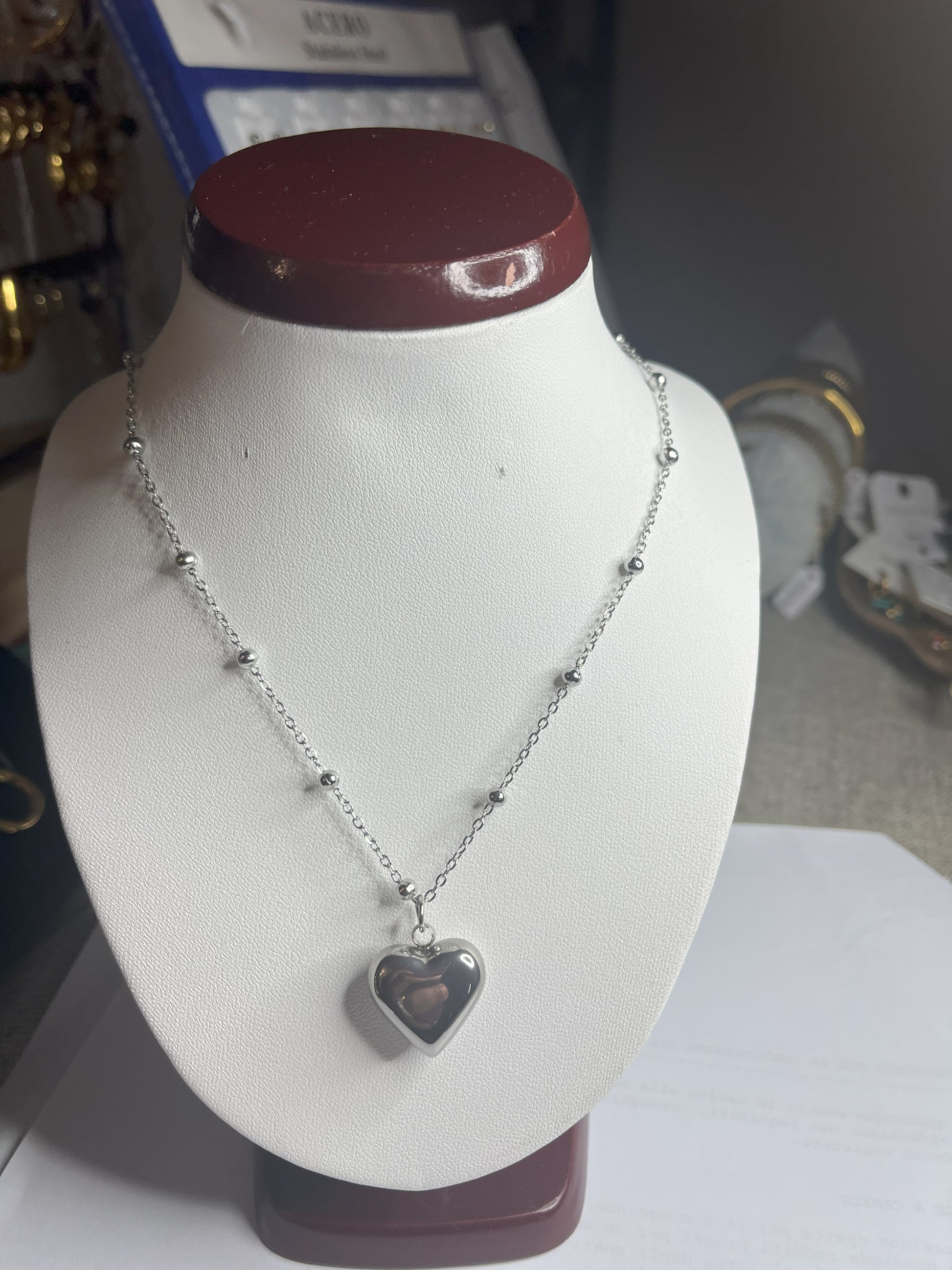 Collana Allegra in acciaio premium con catena decorata da sfere e ciondolo cuore, variante placcato argento, esposta su busto espositore bianco