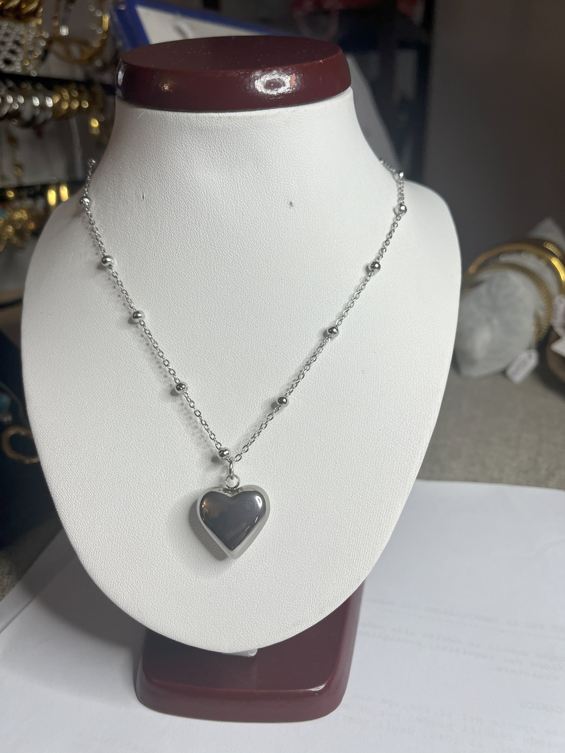 Collana Allegra in acciaio premium con catena decorata da sfere e ciondolo cuore, variante placcato argento, esposta su busto espositore bianco