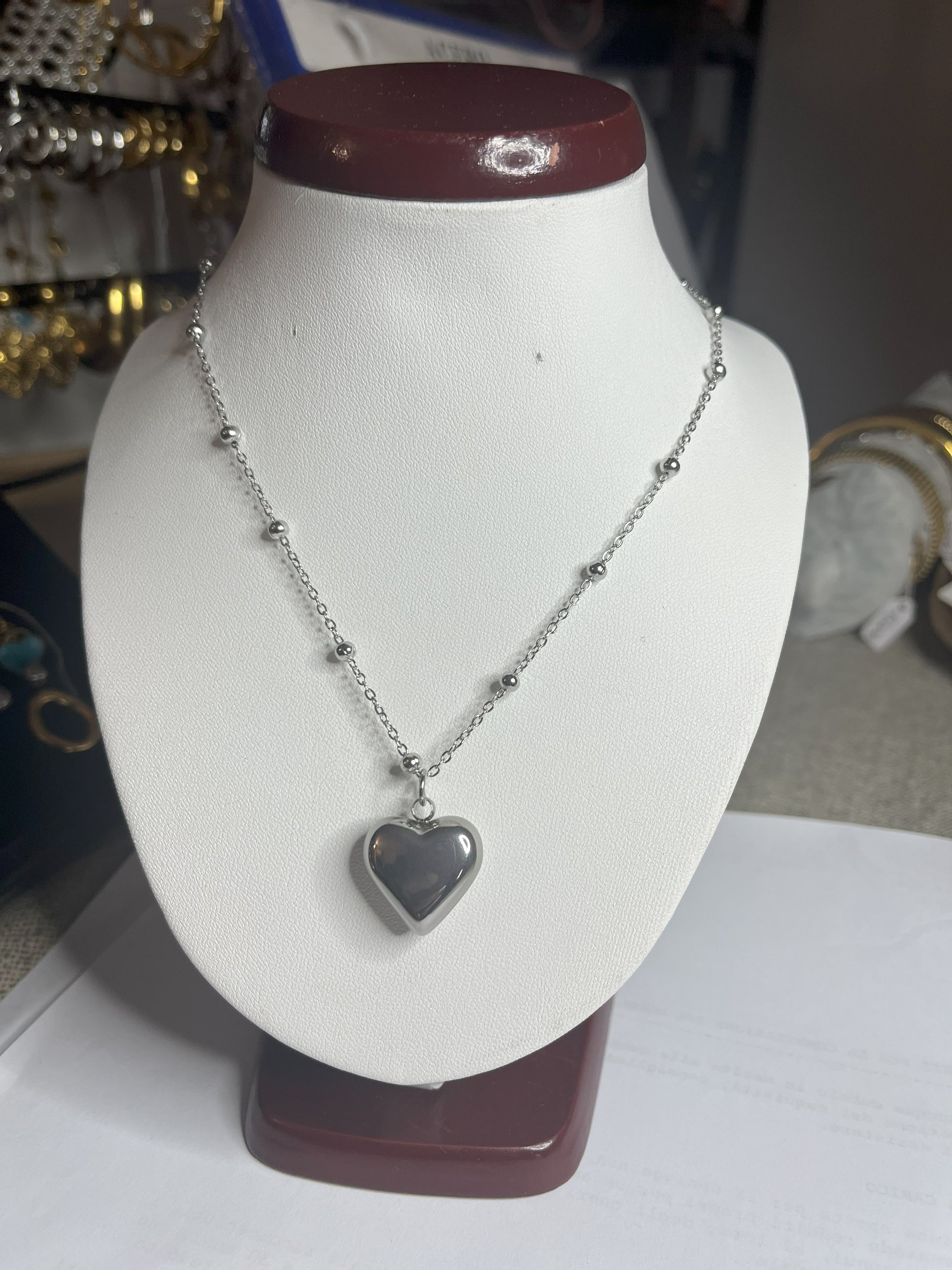 Collana Allegra in acciaio premium con catena decorata da sfere e ciondolo cuore, variante placcato argento, esposta su busto espositore bianco