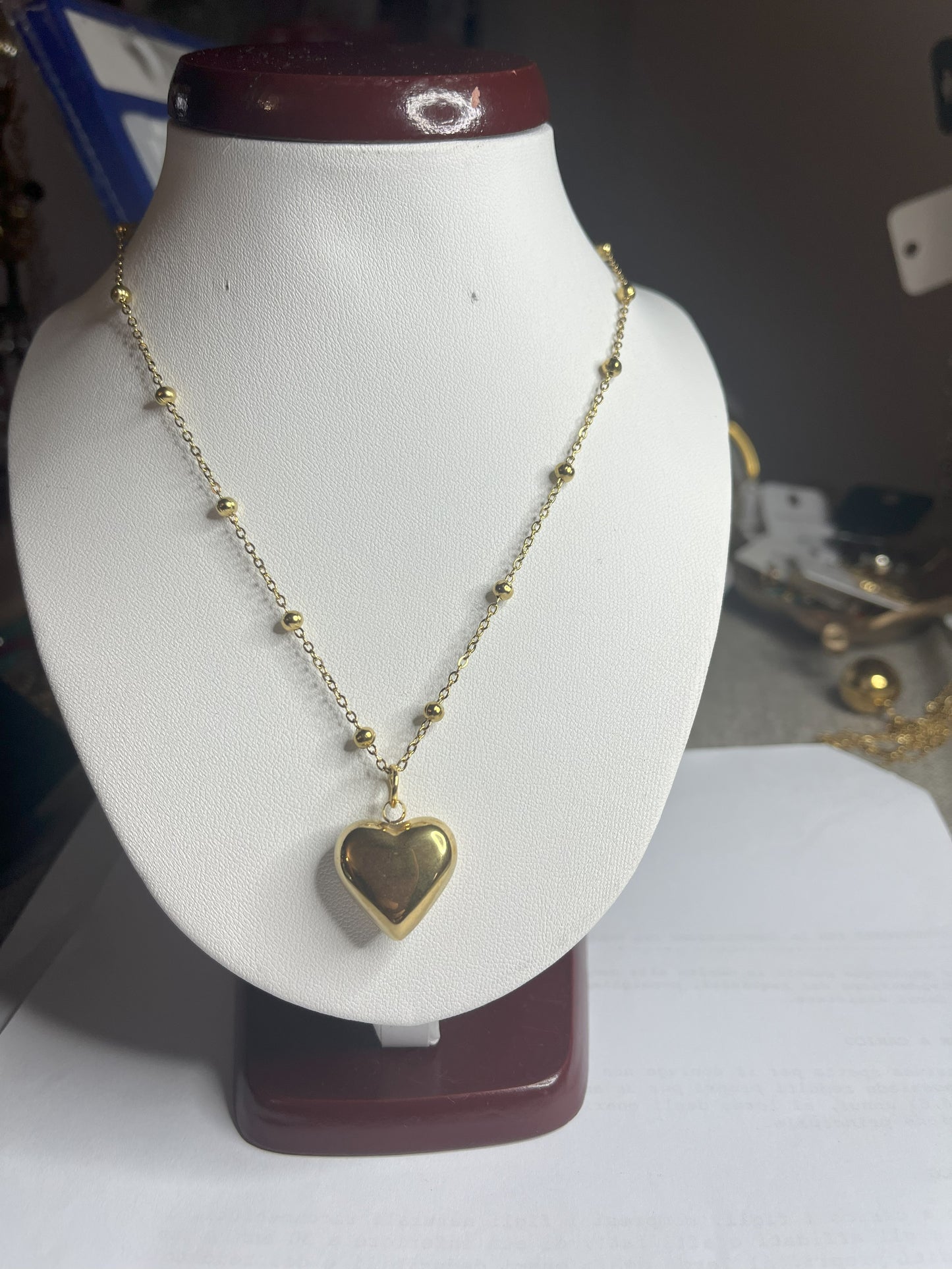 Collana Allegra in acciaio premium con catena decorata da sfere e ciondolo cuore, variante placcato oro, esposta su busto espositore bianco