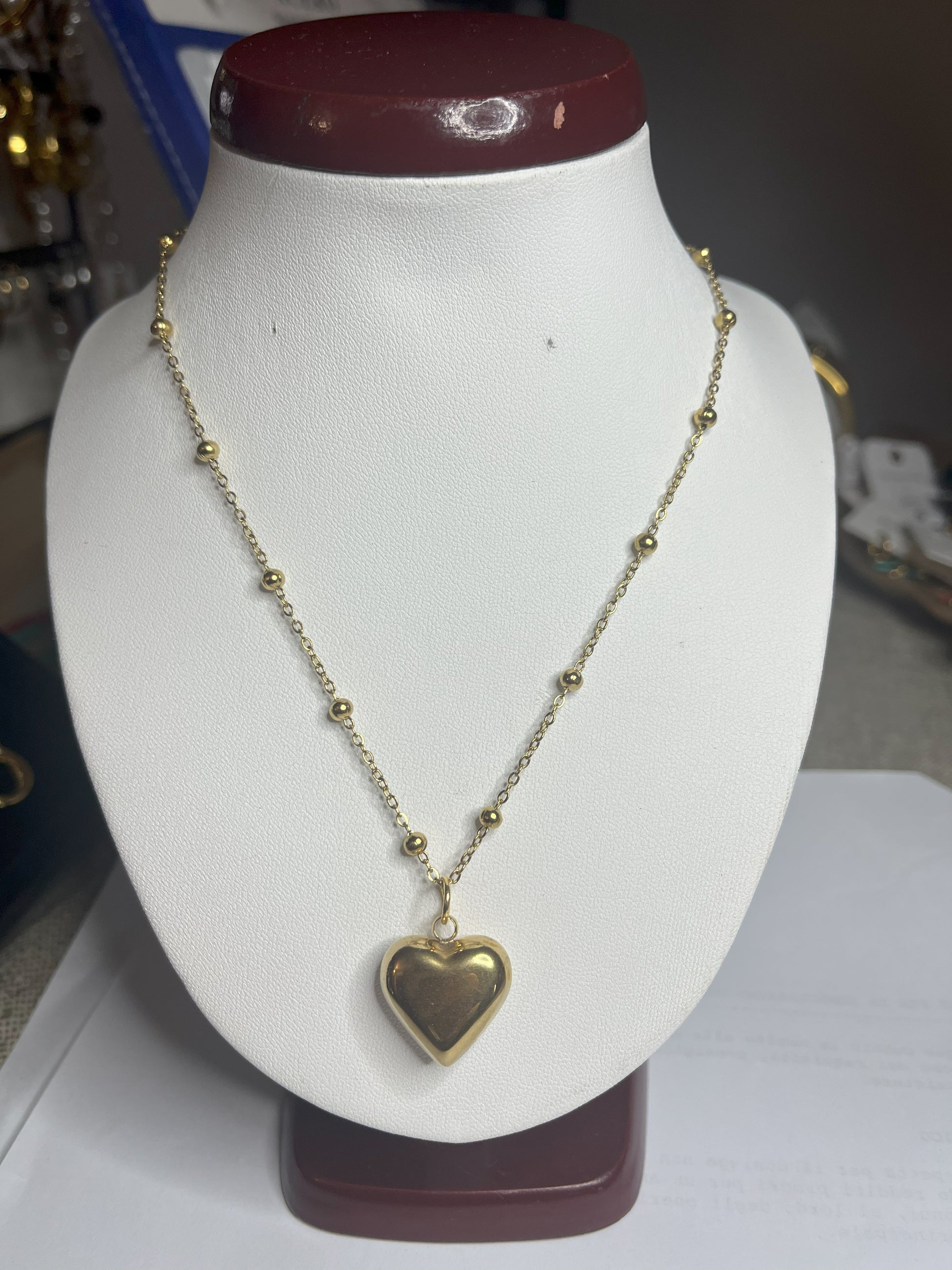 Collana Allegra in acciaio premium con catena decorata da sfere e ciondolo cuore, variante placcato oro, esposta su busto espositore bianco
