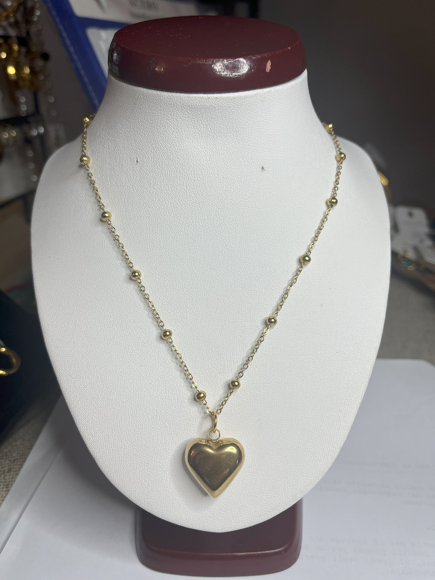 Collana Allegra in acciaio premium con catena decorata da sfere e ciondolo cuore, variante placcato oro, esposta su busto espositore bianco