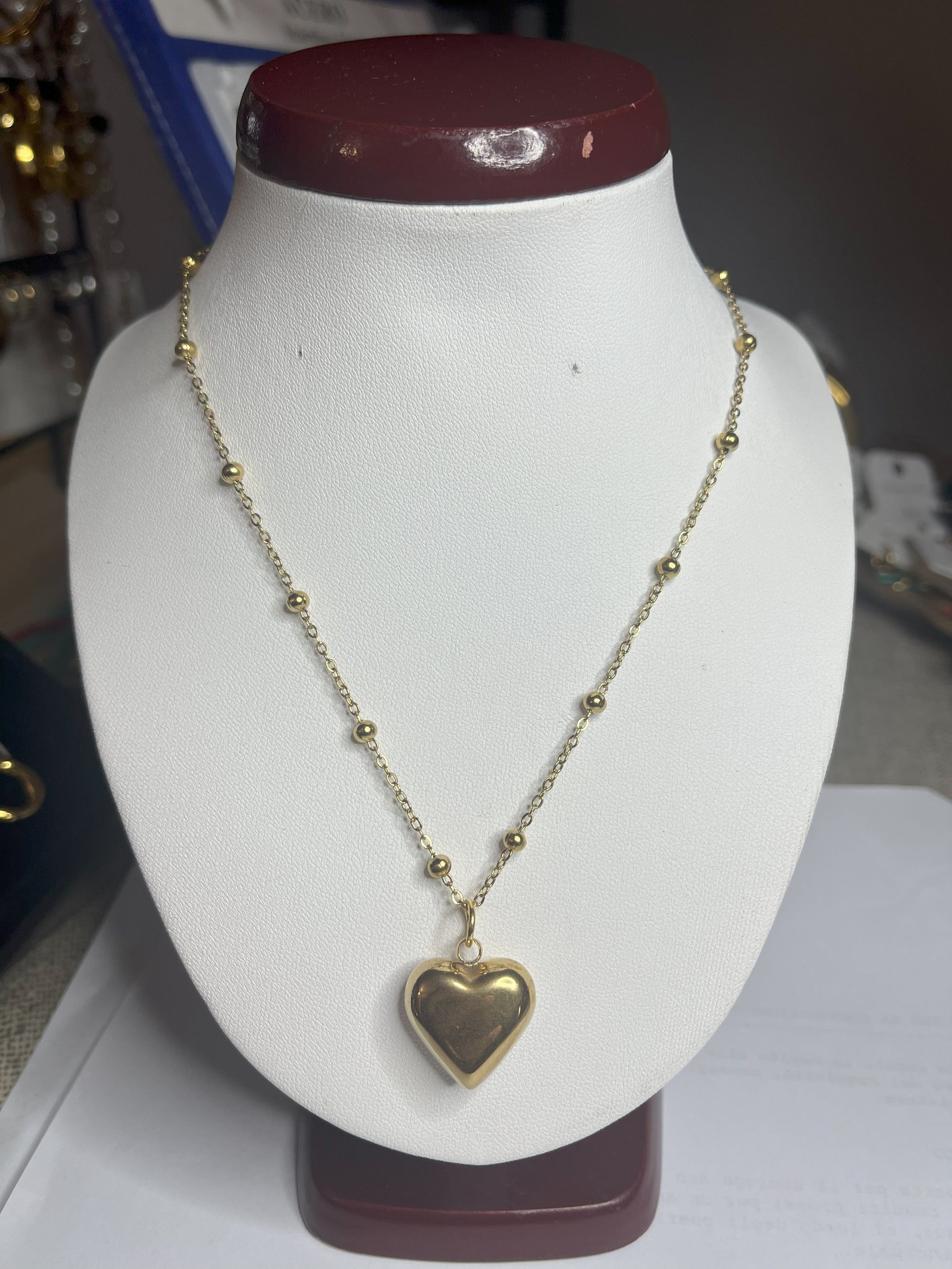 Collana Allegra in acciaio premium con catena decorata da sfere e ciondolo cuore, variante placcato oro, esposta su busto espositore bianco